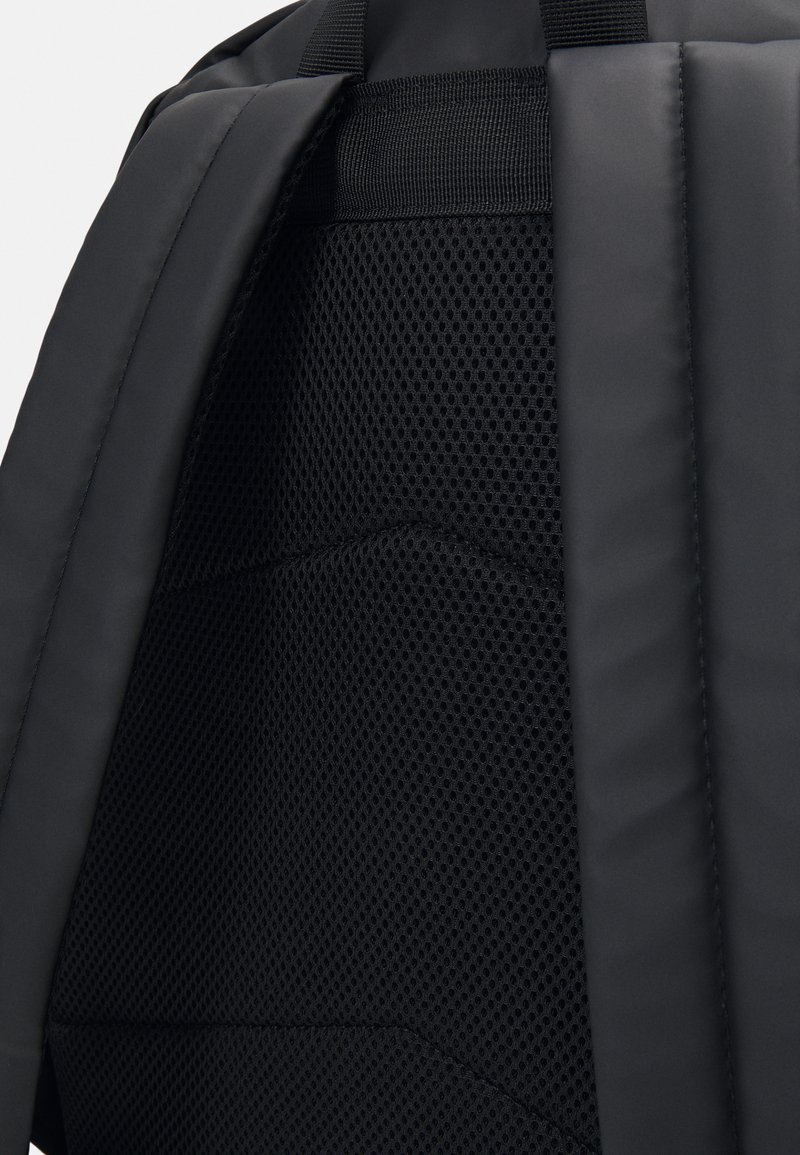 Mochila negra con un exterior acolchado y un panel trasero de malla transpirable para ventilación. Textura suave con costuras planas.