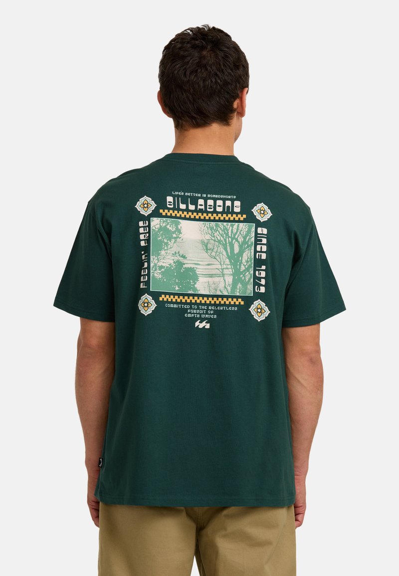 Camiseta de algodón verde oscuro con un estampado gráfico en la parte posterior que presenta diseños geométricos en crema y amarillo, y una imagen central de árboles.