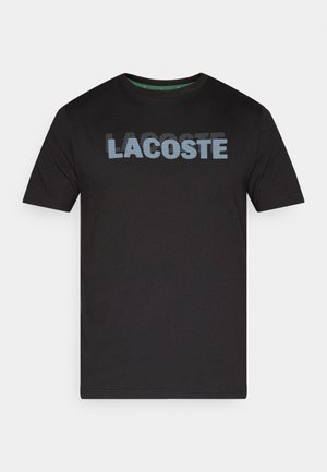 T-shirt nera a maniche corte in cotone, con grande scritta puntinata blu "LACOSTE" sul davanti, collo rotondo.