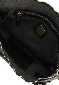 Interno di una borsa nera in tela con tasca con zip, molteplici scomparti, una etichetta e una zip argentata lungo il bordo.