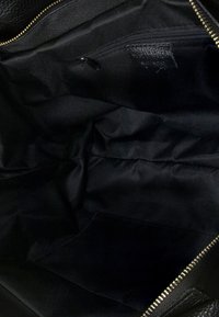 Zwarte leren tote bag interieur met een gladde stoffen voering, een ritssluiting en meerdere compartimenten voor organisatie.