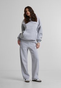 Pilkos medvilnės džemperis su kengūros kišene, derinamas su atitinkančiomis pilkomis sportinėmis kelnėmis su šoninėmis siūlėmis. Apsirengta pilkais ir baltais sportbačiais.