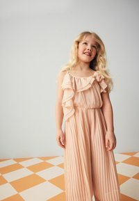 Robe en pêche plissé avec col à volants et bretelles ajustables. Présente une texture douce et une taille élastique pour plus de confort.