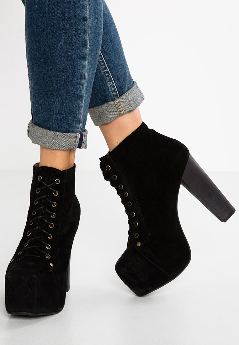 Bottines montantes à lacets en daim noir avec plateforme et talons hauts épais, portées avec un jean bleu retroussé.