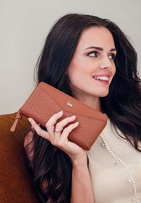 Brown leather wallet with a crocodile texture, featuring a gold logo and a zipper. There is a subtly textured design on the top.