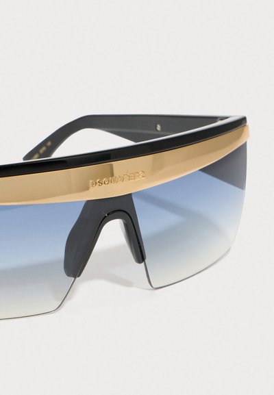 Gafas de sol negras y doradas con una lente grande y curvada que presenta un degradado de ombré de azul a transparente. Las varillas son elegantes y cuentan con un detalle de logo.