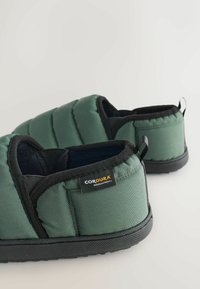 Zelené prešívané papuče z odolnej látky Cordura, s čiernym lemováním a textúrovanou gumovou podrážkou pre lepšiu priľnavosť. Obsahujú aj pútko.