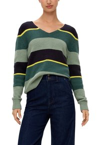 Grüner, marineblauer und gelber gestreifter Strickpullover mit V-Ausschnitt, langen Ärmeln, gerippten Bündchen und entspannter Passform. Kombiniert mit dunklen Jeans.