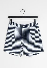 Marinblå och vita randiga shorts med veckad front, knappstängning och rak passform. De hänger från en svart krok på en vit bakgrund.