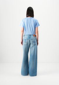 T-shirt bleu clair à manches courtes associé à un jean ample en denim bleu délavé. Le denim présente un design classique à cinq poches et une étiquette en cuir au dos.