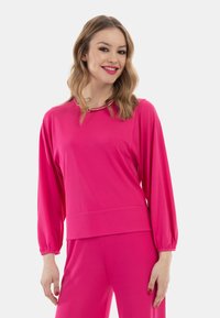 Maglietta fucsia a maniche lunghe con scollo arrotondato, caratterizzata da un dettaglio dorato al collo. Realizzata in un tessuto morbido ed elasticizzato per garantire comfort.