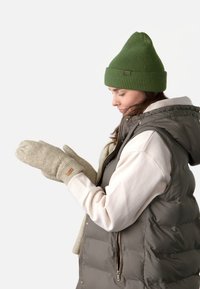 Un bonnet côtelé vert, des mitaines crème avec des motifs de diamants texturés, et un gilet gris matelassé sur un hoodie blanc sont portés par une personne.