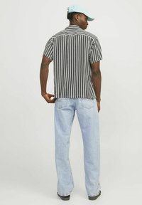 Kortærmet sort-hvid stribet skjorte parret med lyseblå jeans. Skjorten har krave og en afslappet pasform. En lyseblå kasket bæres.