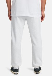 Lichtgrijze sweatpants van zachte stof, met een losse pasvorm, elastische boorden en zijzakken. G gedragen met zwarte sneakers.