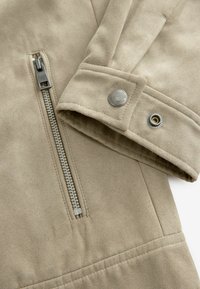 Beige jacket fabric with a soft texture. Features a silver metal zipper, snap fastener, and angled seams for structure.