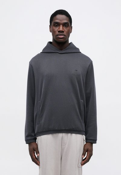 Mørk grå hettegenser med ribbet tekstur, kengurulomme og subtil logo på brystet, brukt med lysegrå bukser.