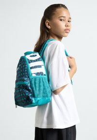 Τουρκουάζ σακίδιο με μοτίβο στο μπροστινό μέρος, πλέγμα στο πλάι, και μαλακή πλάτη. Διαθέτει ρυθμιζόμενους ιμάντες και λαβή στην κορυφή.