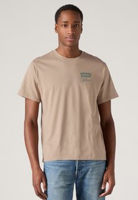 Bezs színű pamut póló rövid ujjakkal és kerek nyakkivágással. A mellkasán egy kis zöld Levi's California logó található.