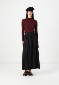 Burgundijas krāsas ribota blūze ar garām piedurknēm un melna maxi svārki ar elastīgu jostasvīru; papildināta ar melnu bereti un zīmējumu slip-on apaviem.