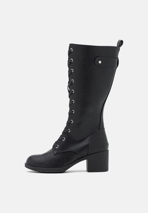 Botte mi-mollet en cuir noir avec laçage à l'avant, talon bloc et détail de sangle latérale sur fond blanc uni.