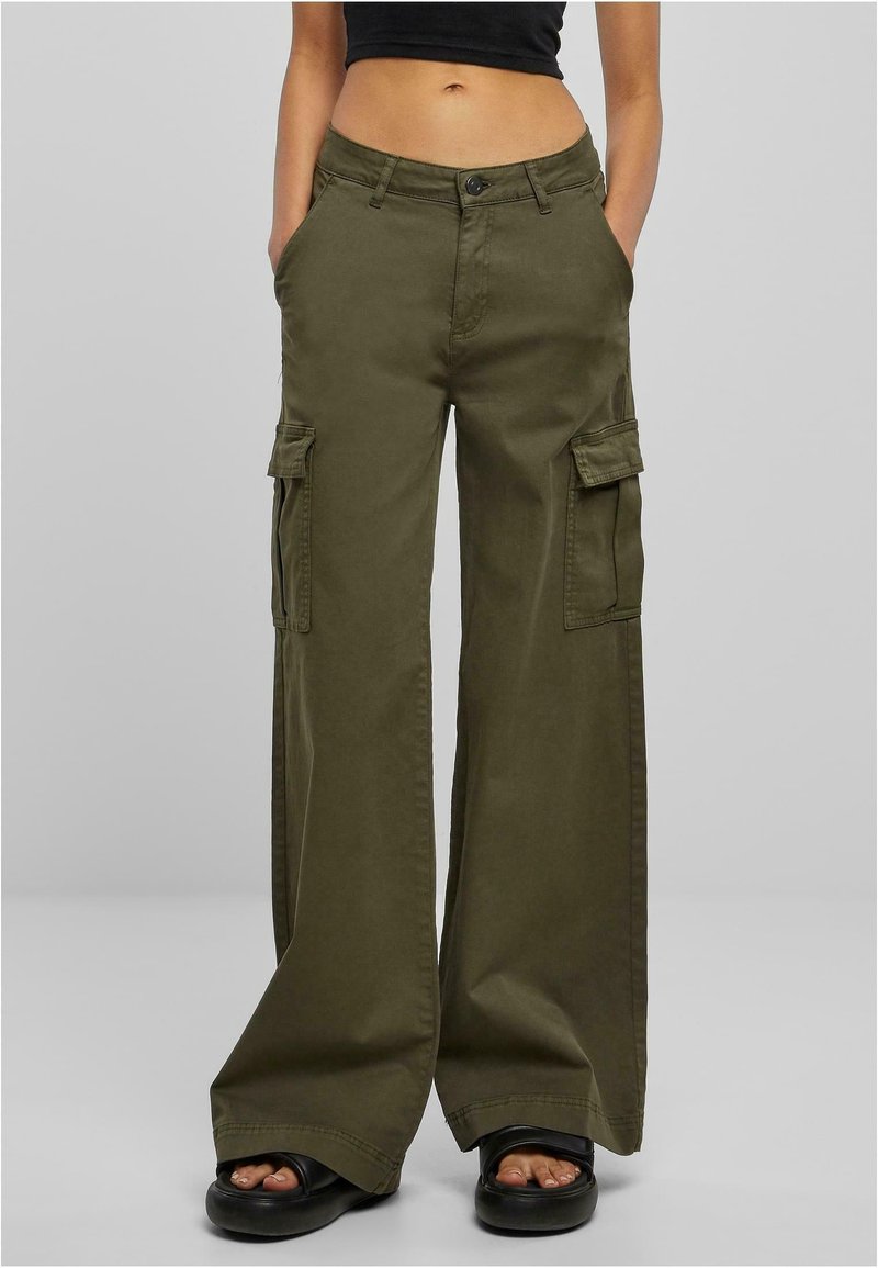 Olijfgroene wijde cargobroek met klepzakken, gedragen met een zwarte cropped top en zwarte platform sandalen, model staat met handen in de zakken.