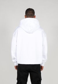 Witte hoodie met een grote achterkap en een oversized pasvorm. Gemaakt van zachte stof. Gecombineerd met donkere cargobroeken. Eenvoudig en minimalistisch ontwerp.
