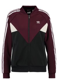 Jacka med dragkedja som har en vinröd överdel, svart underdel och vita triangulära detaljer, samt vita ränder på ärmarna.