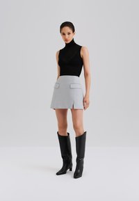 Melnas bezroku augsta kakla augšdaļa, kombinēta ar gaiši pelēku mini svārku ar divām priekšējām kabatām. Melnas ceļgalu augstās zābaki ar papēžiem pabeidz izskatu.