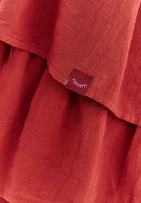 Červená textúrovaná tkanina s malou prišitou nálepkou zobrazujúcou biely symbol zatvoreného oka.