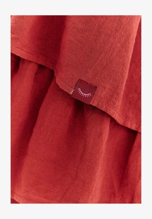 Červená textúrovaná tkanina s malou prišitou nálepkou zobrazujúcou biely symbol zatvoreného oka.