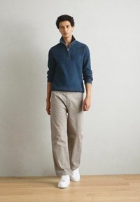 Marineblauer Reißverschluss-Pullover, beiges Hosen und weiße Sneakers. Der Pullover hat einen Stehkragen und gerippte Bündchen, was einen lässigen Look erzeugt.