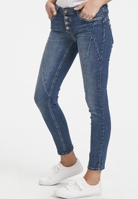 Vaqueros de mezclilla azul con cintura alta, cierre de cinco botones y un ligero desvanecimiento. Presentan un ajuste slim y costuras curvas para un aspecto ajustado.