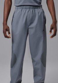 Szare spodnie sportowe z elastycznym pasem, bocznymi kieszeniami oraz wzorem w kropki wzdłuż nóg. Na udzie znajduje się logo Jordan.