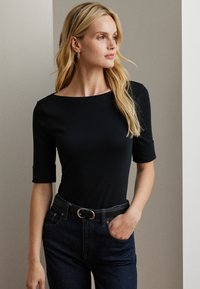 Zwarte fitted top met een bootnek en driekwartmouwen, gecombineerd met donkere denim jeans en een zwarte riem met een ronde gesp.