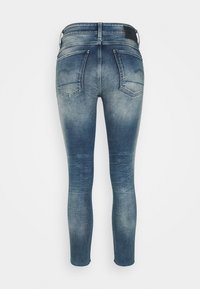 Jeans de denim ajustados en un degradado azul, con cintura alta, dos bolsillos traseros y un leve desvanecimiento en las piernas inferiores.