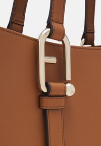 Borsa a mano in pelle marrone con dettaglio della chiusura in ottone dorato. Caratterizzata da manici robusti con cuciture a contrasto e una superficie liscia.
