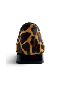 Chaussure à motif léopard avec une texture de fourrure douce, une base noire brillante, une forme arrondie, un talon anglé et des taches sombres distinctes sur un fond beige.