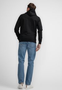 Sudadera negra con capucha y mangas largas, combinada con jeans de mezclilla azul claros y zapatillas blancas. Diseño sencillo sin logotipos ni patrones visibles.