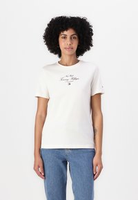 Kortærmet cremet t-shirt i bomuld med "New York Tommy Hilfiger" trykt i brunt, med et lille logo på venstre bryst.