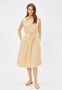 Vestido de manga corta, abotonado, en rayas amarillas y blancas, con cintura ajustada y cinturón, que cuenta con bolsillos laterales y una longitud midi fluida.