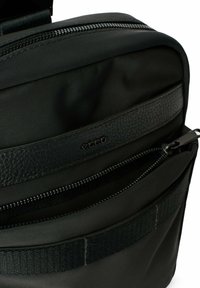 Borsa nera realizzata con una combinazione di nylon liscio e pelle testurizzata. Include diverse tasche con zip e una tracolla robusta.