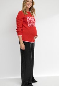 Czerwona sweter robiony na drutach z różowym napisem "BABY IT'S COLD OUTSIDE" w połączeniu z błyszczącymi czarnymi spodniami z szerokimi nogawkami pokrytymi cekinami. Gładka tekstura i dopasowany krój.