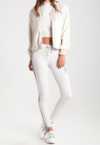 Lightweight cream bomber jacket over a white cropped top, paired with gray leggings featuring black side stripes and white sneakers.
