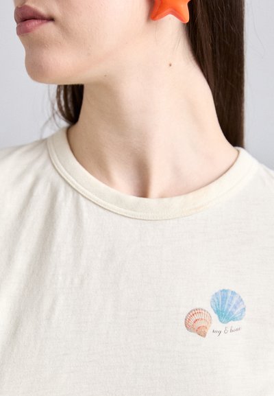 Cremfarbener T-Shirt mit einer zarten Grafik von zwei Muscheln in Pastellfarben, mit dem Text "rag & bone" unter den Muscheln.