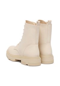 Beżowe sznurowane botki z gładkiej skóry, o wysokim fasonie i grubych gumowych podeszwach. Posiadają wzmocniony tył i minimalne detale szycia.