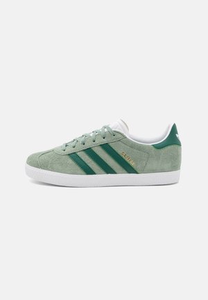 Baskets Adidas Gazelle vert clair avec des bandes vert foncé, semelle blanche et doublure intérieure blanche, vues de côté sur un fond uni.