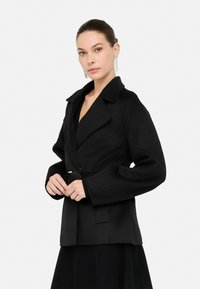 Chaqueta negra envolvente con cuello ancho, mangas largas y cierre con cinturón. Tejido texturizado con un acabado suave, que incluye bolsillos laterales.
