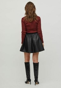 Top de manga larga con rayas rojas y negras, combinado con una falda acampanada de cuero sintético negra y botas negras hasta la rodilla con tacones puntiagudos.