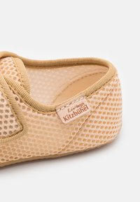 Beige nättoffel med en strukturerad yta, rund form och mjuk kant. Har en etikett med "Living Kitzbühel"-logotyp.