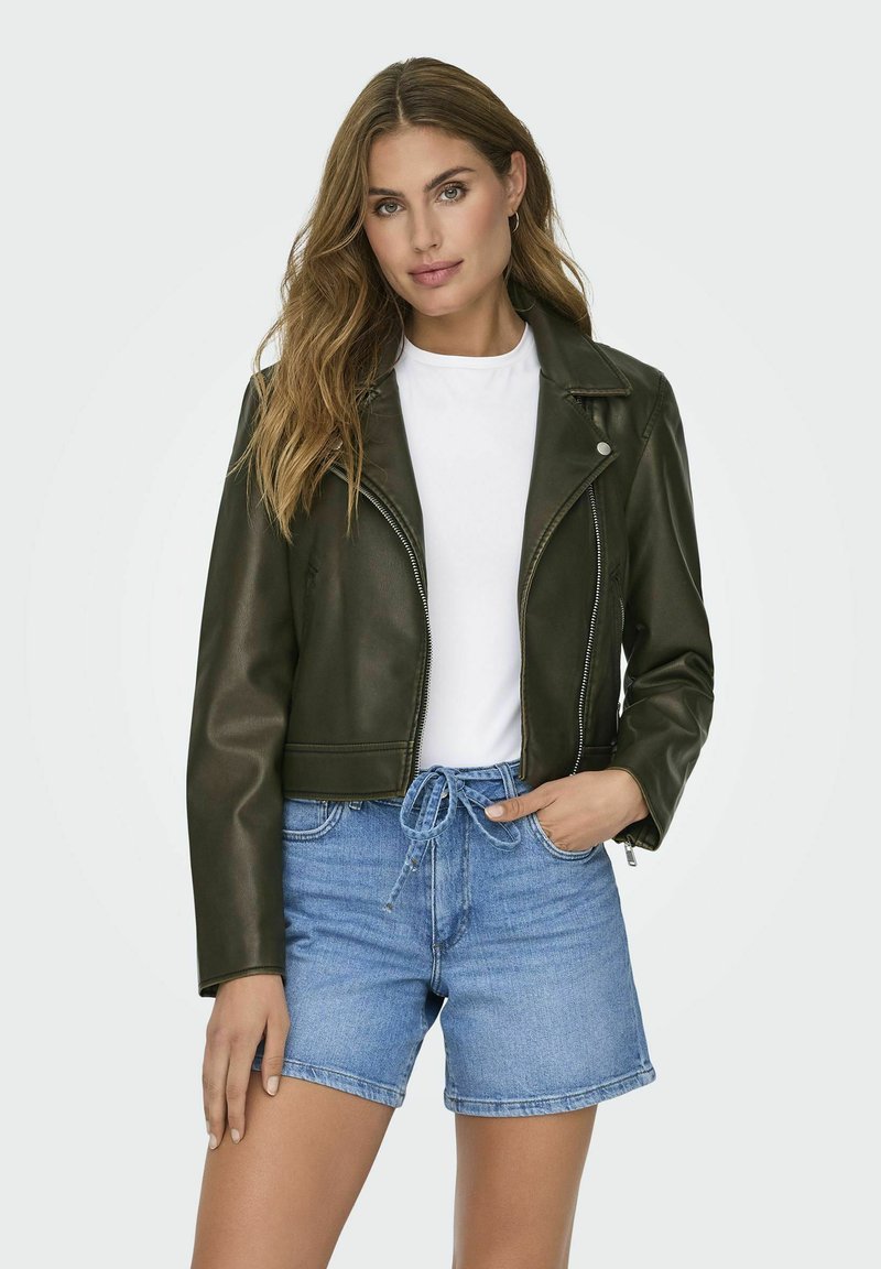 Giacca in pelle verde oliva tagliata, con chiusura a zip, colletto a rever e spalline, indossata sopra una t-shirt bianca e pantaloni corti blu.